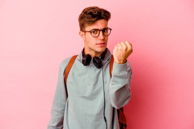Pembe arka planda izole edilmiş genç bir öğrenci kameraya yumruğunu gösteriyor, agresif yüz ifadesi..