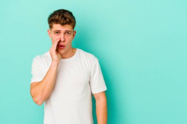 Mavi arka planda izole edilmiş genç beyaz bir adam gizli bir sıcak fren haberi veriyor ve yana bakıyor.