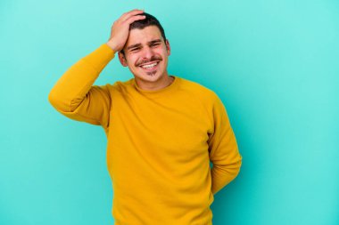 Mavi arka planda izole edilmiş genç beyaz bir adam zaferi, tutkuyu ve coşkuyu kutluyor, mutlu bir ifade..