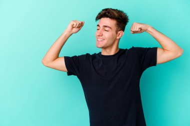 Mavi arka planda izole edilmiş genç beyaz bir adam zaferden sonra yumruğunu kaldırıyor, kazanan konsept..