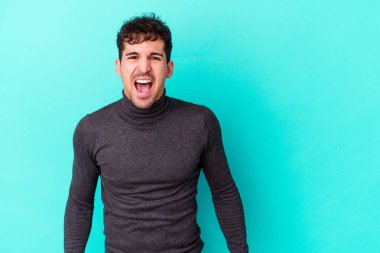 Kafkasyalı genç adam mavi arka planda izole edilmiş. Çok kızgın, öfkeli, hayal kırıklığına uğramış..