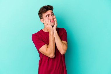 Kafkasyalı genç adam mavi arka planda izole edilmiş sızlanıyor ve ağlıyordu..