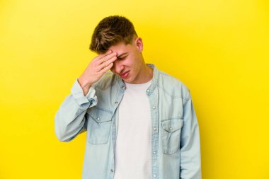 Sarı arka planda izole edilmiş genç beyaz adam kameraya parmaklarıyla göz kırpıyor, yüzünü kapatmaktan utanıyor..