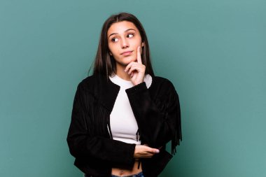 Mavi arka planda izole edilmiş genç Hintli kadın şüpheli ve şüpheci bir ifadeyle yana bakıyor..