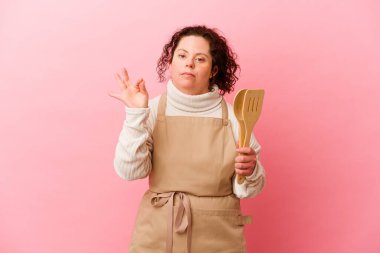 Down sendromlu kadın evde yemek pişiriyor pembe arka planda izole edilmiş neşeli ve kendinden emin..