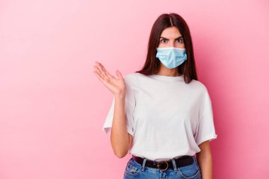 Pembe arka planda izole edilmiş virüs maskesi takan beyaz bir kadın avuç içinde kopya alanı tutmaktan etkilenmiş..