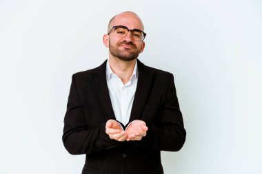 Genç beyaz, kel bir adam mavi arka planda izole edilmiş. Elinde avuç içi olan bir şey var. Kameraya teklif ediyor..