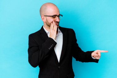 Genç, beyaz, kel bir adam mavi arka planda izole edilmiş. Dedikodu yapıyor, bir şeyleri bildiriyor..