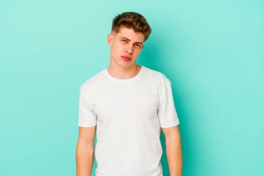 Kafkasyalı genç adam mavi arka planda izole edilmiş üzgün, ciddi yüzlü, mutsuz ve hoşnutsuz..