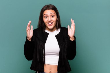 Genç Hintli kadın mavi arka planda izole edilmiş. Hoş bir sürpriz bekliyor. Heyecanlı ve el kaldırıyor..