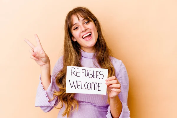 Young caucasian woman holding a Refugees welcome placard isolated joyful and carefree showing a peace symbol with fingers.