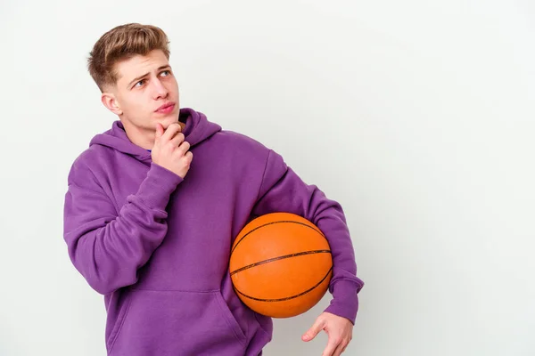 若いですCaucasian男遊びバスケットボール隔離された背景見て横にとともに疑問と懐疑的な表現 — ストック写真
