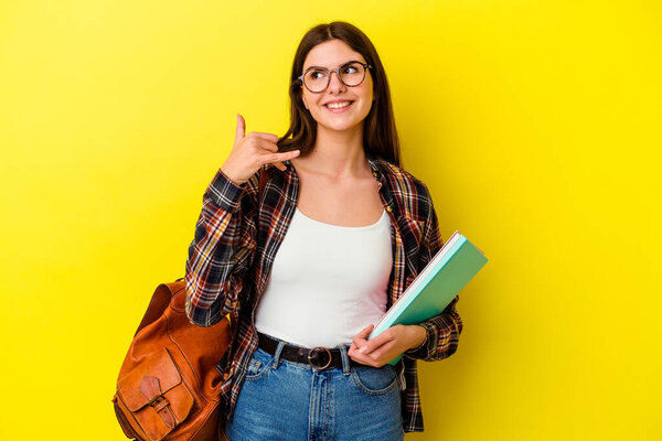 Young student woman isolated on yellow background showing a mobile phone call gesture with fingers.