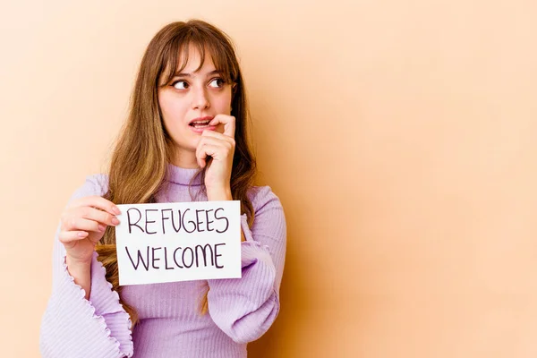 Young caucasian woman holding a Refugees welcome placard isolated relaxed thinking about something looking at a copy space.