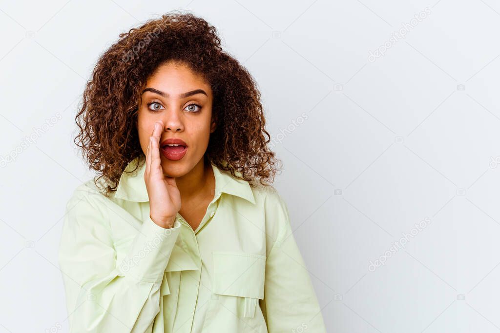 Young african american woman isolated on white background is saying a secret hot braking news and looking aside