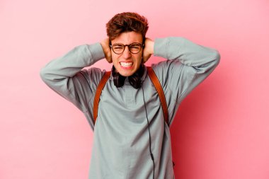 Pembe arka planda izole edilmiş genç bir öğrenci kulakları elleriyle kapatıyor ve yüksek sesle sesler duymamaya çalışıyor..