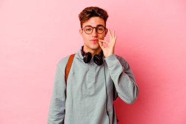 Pembe arka planda izole edilmiş genç bir öğrenci dudaklarında parmaklarıyla bir sır saklıyor..