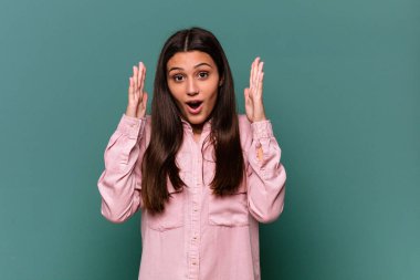 Genç Hintli kadın mavi arka planda zaferi ya da başarıyı kutlarken şaşırdı ve şok oldu..