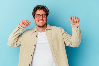 Gözlüklü genç beyaz adam mavi arka planda izole edilmiş dans ediyor ve eğleniyor..