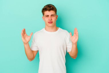 Kafkasyalı genç adam mavi arka planda izole edilmiş. Elinde işaret parmaklarıyla küçük bir şey tutuyor, gülümsüyor ve kendinden emin..
