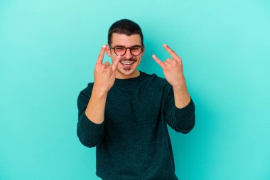 Mavi arka planda izole edilmiş genç beyaz adam boynuzlarını devrim konsepti olarak gösteriyor..