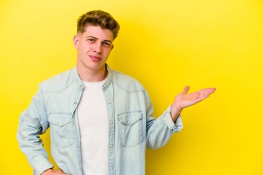 Sarı arka planda izole edilmiş genç beyaz bir adam bir palmiye üzerinde fotokopi alanı gösteriyor ve belinde başka bir el tutuyor..