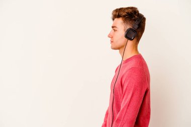 Beyaz arka planda yalnız başına müzik dinleyen beyaz bir adam sola bakıyor, yan pozlar veriyor..