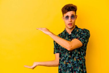 Sarı arka planda izole edilmiş Hawaii tişörtü giyen genç beyaz adam elleri arasında bir fotokopi alanı tutarken şok ve hayrete düştü..