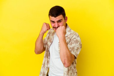 Sarı arka planda izole edilmiş genç beyaz adam kameraya yumruğunu gösteriyor, agresif yüz ifadesi..