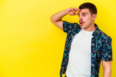 Kafkas asıllı genç adam sarı arka planda izole edilmiş, uzaklara bakıyor ve elini alnına koyuyor..