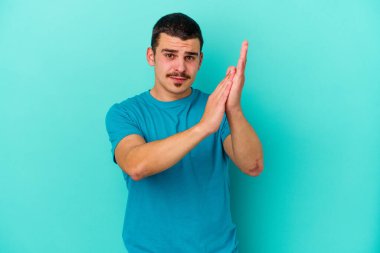 Kafkasyalı genç adam mavi arka planda izole edilmiş enerjik ve rahat hissediyor, ellerini ovuşturuyor kendinden emin.