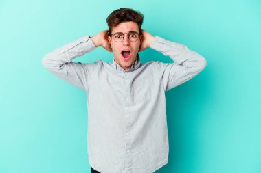 Mavi arka planda izole edilmiş genç beyaz adam öfkeyle bağırıyor..
