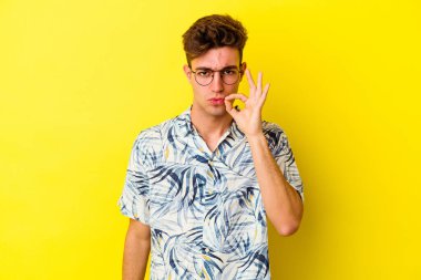 Sarı arka planda izole edilmiş genç beyaz bir adam parmakları dudaklarında bir sır saklıyor..