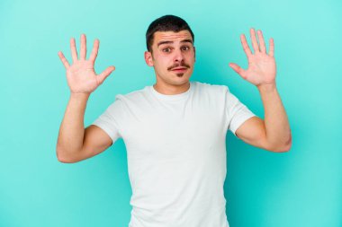 Kafkasyalı genç adam mavi arka planda izole edilmiş gökyüzüne haykırıyor, yukarı bakıyor, hayal kırıklığına uğramış..