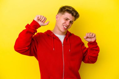 Sarı arka planda izole edilmiş genç beyaz adam özel bir günü kutluyor, atlıyor ve enerjiyle kollarını kaldırıyor..