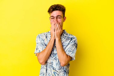 Sarı arka planda izole edilmiş genç beyaz bir adam bir şeye gülüyor, ağızlarını ellerle kapatıyor..