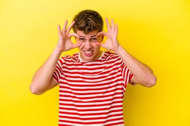 Sarı arka planda izole edilmiş genç beyaz adam bir başarı fırsatı bulmak için gözlerini açık tutuyor..