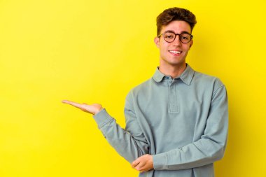 Sarı arka planda izole edilmiş genç beyaz bir adam bir palmiye üzerinde fotokopi alanı gösteriyor ve belinde başka bir el tutuyor..