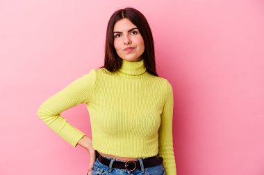 Pembe arka planda izole edilmiş genç beyaz kadın kafası karışmış, kuşkulu ve güvensiz hissediyor..