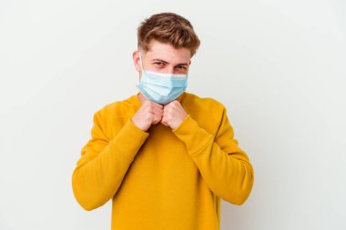 Beyaz arka planda izole edilmiş Coronavirus maskesi takan genç adam ellerini çenesinin altında tutuyor ve mutlu bir şekilde yan tarafa bakıyor..
