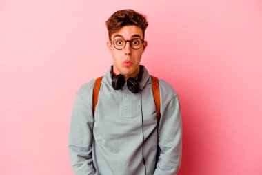 Pembe arka planda izole olmuş genç bir öğrenci omuz silkiyor ve gözleri açık..