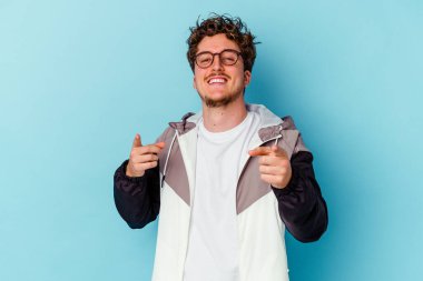 Gözlük takan genç beyaz adam mavi arka planda izole edilmiş önü işaret eden neşeli gülümsemeler..
