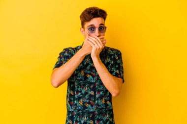 Sarı arka planda izole edilmiş Hawaii tişörtü giyen genç beyaz adam elleri ile ağzını kapatırken şok oldu..