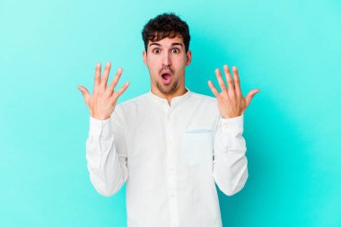 Mavi arka planda izole edilmiş genç beyaz adam on numarayı elleriyle gösteriyor..