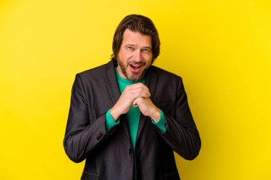 Orta yaşlı beyaz bir adam sarı arka planda izole edilmiş şans için dua ediyor, şaşırmış ve ağzını açıp önüne bakıyor..