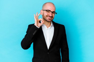 Genç beyaz tenli kel adam mavi arka planda izole edilmiş neşeli ve kendine güvenen iyi bir hareket sergiliyor..