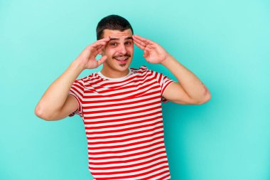 Mavi arka planda izole edilmiş genç beyaz adam hoş bir sürpriz alıyor, heyecanlı ve el kaldırıyor..