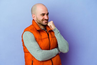 Kafkasyalı kel adam mor arka planda izole edilmiş mutlu ve kendinden emin gülümsüyor, elleriyle çenesine dokunuyor..