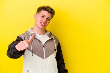 Sarı arka planda izole edilmiş genç beyaz adam gülümsüyor ve başparmağını kaldırıyor.