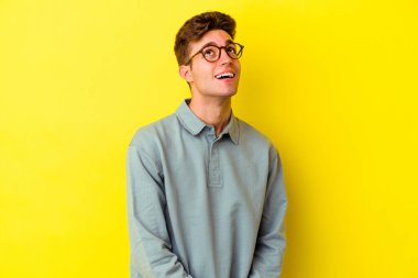 Sarı arka planda izole edilmiş genç beyaz adam gevşemiş ve mutlu gülüyor, boynunda dişlerini gösteriyor..